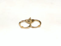 In the center: a 14 karat yellow gold pair of handcuffs pendant laying flat - Popular Jewelry
