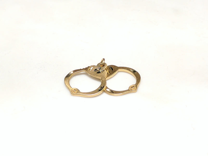 In the center: a 14 karat yellow gold pair of handcuffs pendant laying flat - Popular Jewelry